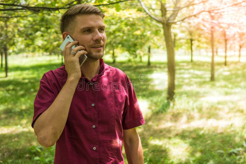 Mężczyzna mówienie na telefonie komórkowym w parku Młody atrakcyjny mężczyzna w obrazy stock Mężczyzna mówienie na telefonie komórkowym w parku Młody atrakcyjny mężczyzna w obrazy stock