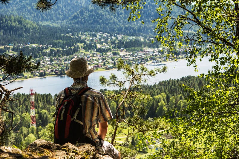 The young man sits and looks from above at the mountain lake. The young man sits and looks from above at the mountain lake