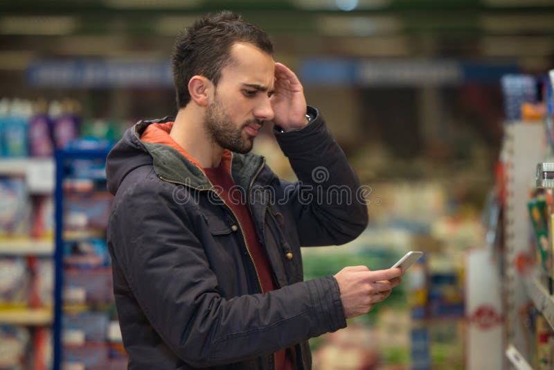 Mężczyzna Patrzeje Wprawiać w zakłopotanie Przy telefonem komórkowym W supermarkecie fotografia stock Mężczyzna Patrzeje Wprawiać w zakłopotanie Przy telefonem komórkowym W supermarkecie fotografia stock