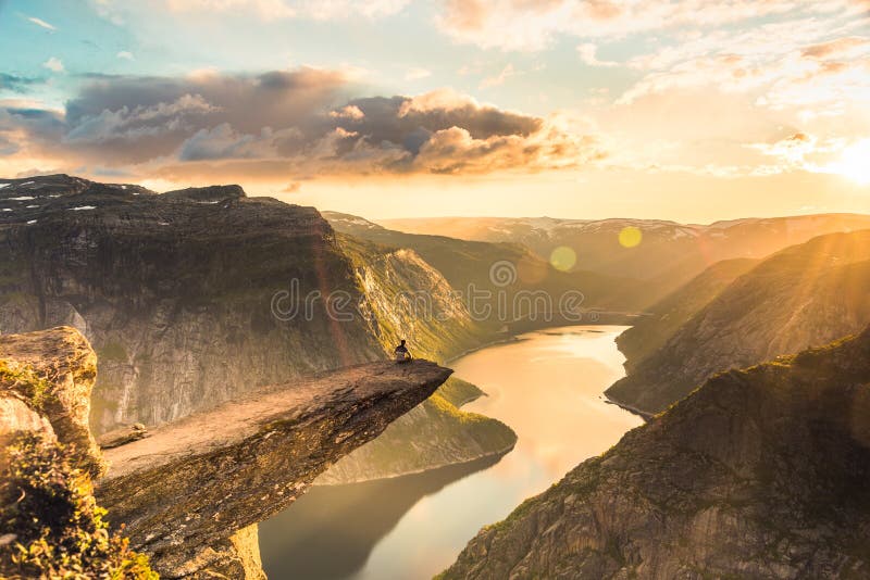 02/09-17, Trolltunga, Norway. A man is sitting on the edge of trolltunga facing the sun. The drop down is 700 m. 02/09-17, Trolltunga, Norway. A man is sitting on the edge of trolltunga facing the sun. The drop down is 700 m