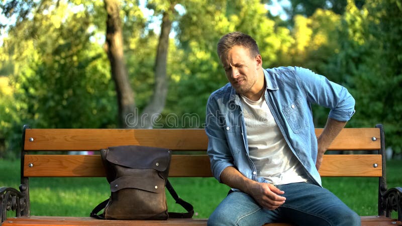 Male sitting on bench suffering from lover back pain after trauma or injury, stock photo. Male sitting on bench suffering from lover back pain after trauma or injury, stock photo