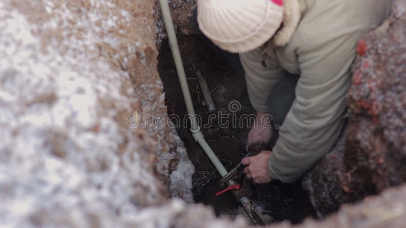 Mężczyzna w dziurze w ziemi i robić nagły wypadek naprawie system wodny Hydraulik pracuje z popielatą klingeryt drymbą