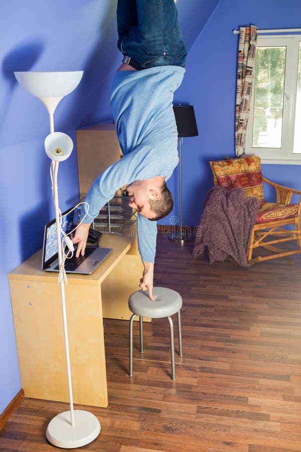 Man in jeans standing upside down under the table with computer. Man in jeans standing upside down under the table with computer