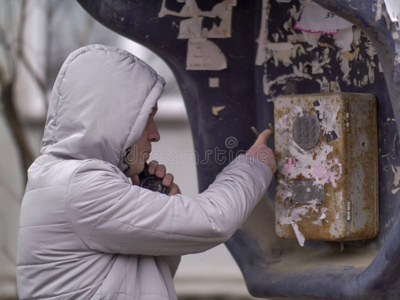 Mężczyzna w lekkiej kurtce w kapiszonie dzwoni starego payphone zdjęcia stock Mężczyzna w lekkiej kurtce w kapiszonie dzwoni starego payphone zdjęcia stock