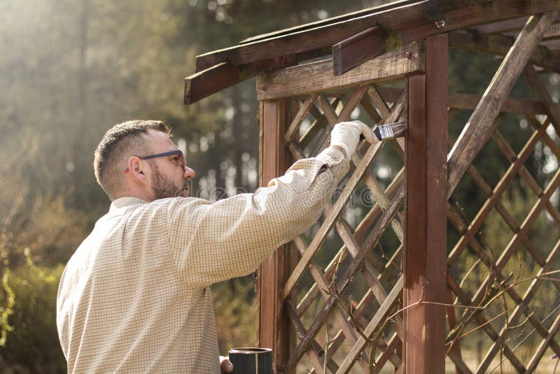 The man in the garden paints brown wooden boards of the garden furniture. Renovation and maintenance of garden pergolas . The man in the garden paints brown wooden boards of the garden furniture. Renovation and maintenance of garden pergolas .