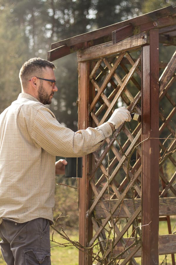 The man in the garden paints brown wooden boards of the garden furniture. Renovation and maintenance of garden pergolas . The man in the garden paints brown wooden boards of the garden furniture. Renovation and maintenance of garden pergolas .