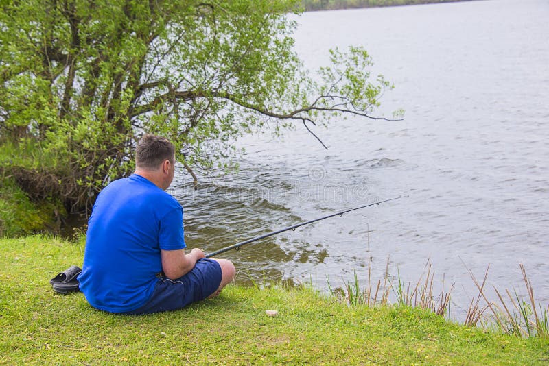 A man with a fishing rod fishing in the pond, on a Sunny lake sitting on the shore. A man with a fishing rod fishing in the pond, on a Sunny lake sitting on the shore