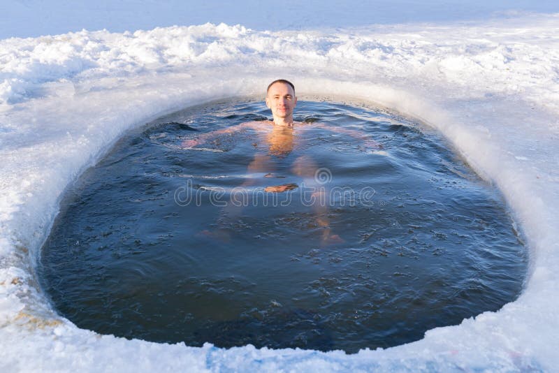 A man relaxes while swimming in a cold hole in ice water in winter. A man relaxes while swimming in a cold hole in ice water in winter.