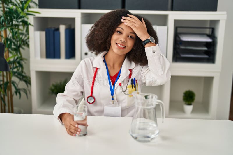 Young african american doctor woman drinking water at the clinic stressed and frustrated with hand on head, surprised and angry face. Young african american doctor woman drinking water at the clinic stressed and frustrated with hand on head, surprised and angry face