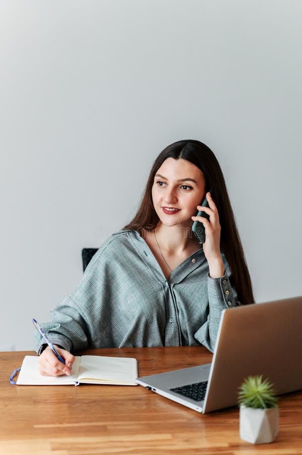 Young woman at the office. She speaks on the phone and writes some information in a notebook. Young woman at the office. She speaks on the phone and writes some information in a notebook