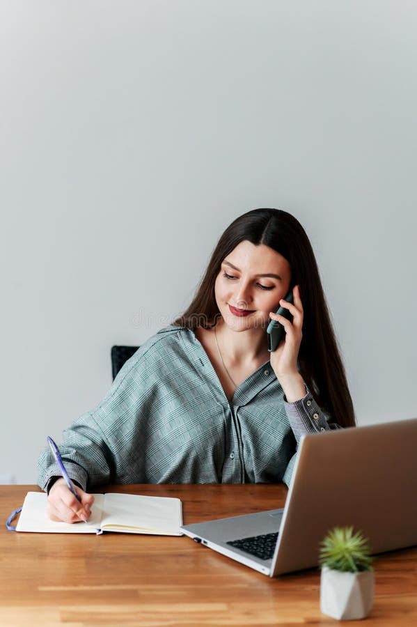 Young woman at the office. She speaks on the phone and writes some information in a notebook. Young woman at the office. She speaks on the phone and writes some information in a notebook