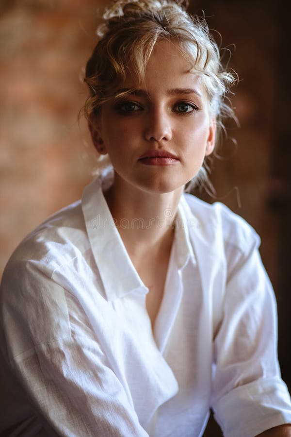 Young blonde woman in a casual white shirt and jeans in a loft interior, close up fashion portrait. Care and beauty. Young blonde woman in a casual white shirt and jeans in a loft interior, close up fashion portrait. Care and beauty