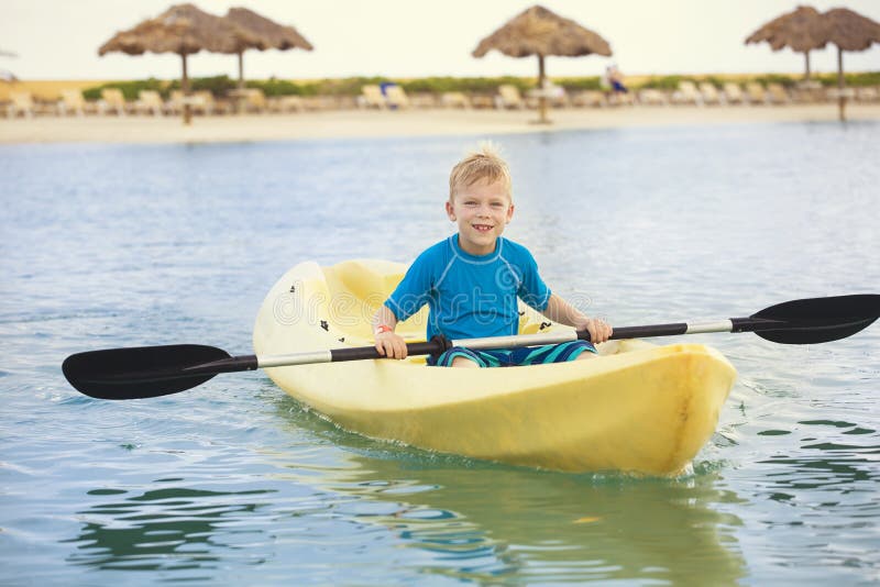 Młoda chłopiec paddling kajaka przy plażą na wakacje zdjęcie stock Młoda chłopiec paddling kajaka przy plażą na wakacje zdjęcie stock