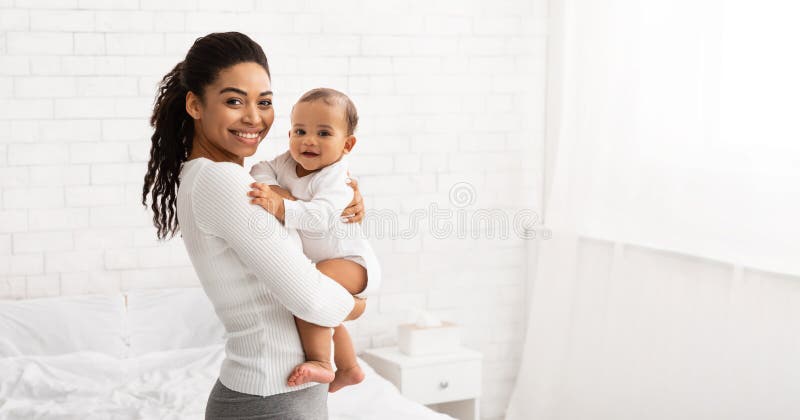Młoda czarna matka trzymająca dziecko w pozycji stojącej w pomieszczeniach panorama