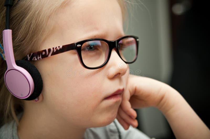 Front view of a young cute girl wearing eyeglasses, looking attentively at laptop computer screen reflected in the lenses. Front view of a young cute girl wearing eyeglasses, looking attentively at laptop computer screen reflected in the lenses.