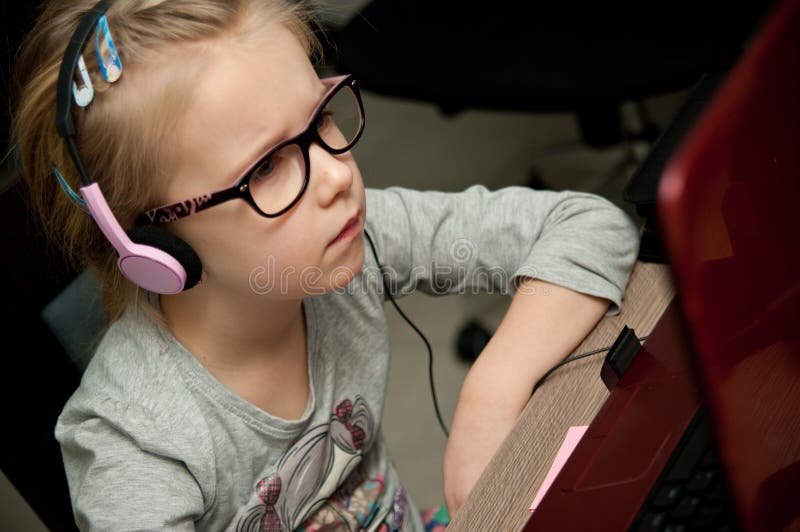 Front view of a young cute girl wearing eyeglasses, looking attentively at laptop computer screen reflected in the lenses. Front view of a young cute girl wearing eyeglasses, looking attentively at laptop computer screen reflected in the lenses.