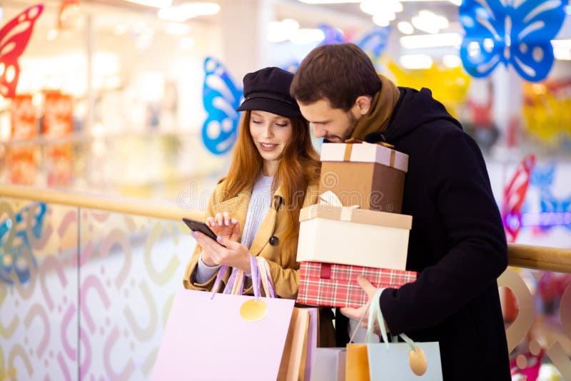 Młoda kaukaska para ze smartfonem w centrum handlowym zdjęcie stock Młoda kaukaska para ze smartfonem w centrum handlowym zdjęcie stock