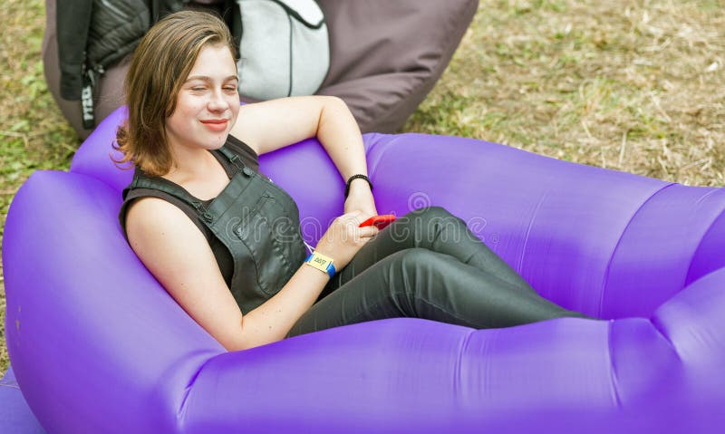KIEV, UKRAINE - JULY 04, 2018: Young beautiful smiling woman dressed in summer clothes sitting in inflatable chair outdoor at the Atlas Weekend Festival in National Expocenter. KIEV, UKRAINE - JULY 04, 2018: Young beautiful smiling woman dressed in summer clothes sitting in inflatable chair outdoor at the Atlas Weekend Festival in National Expocenter