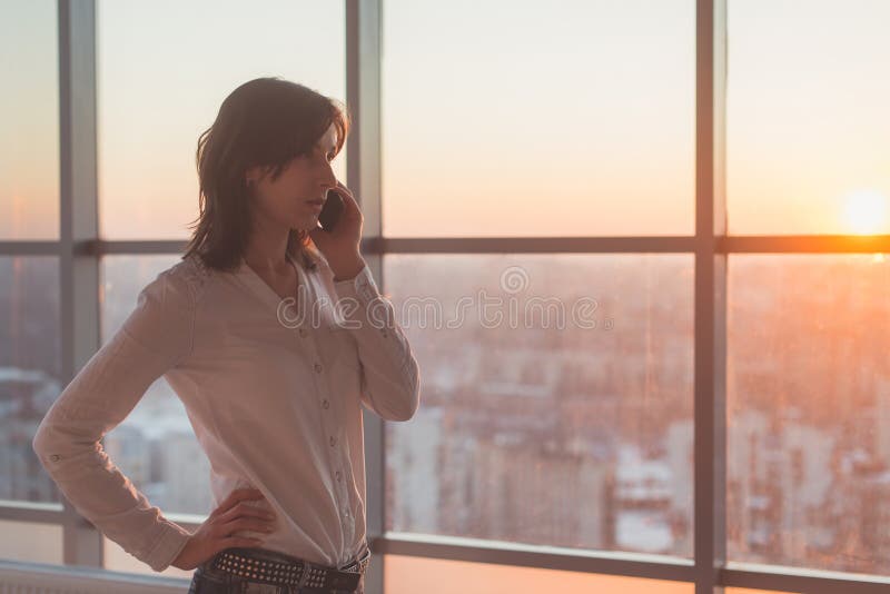 Młoda kobieta opowiada używać telefon komórkowego przy biurem w wieczór Żeński bizneswoman koncentrujący, patrzejący naprzód obraz stock Młoda kobieta opowiada używać telefon komórkowego przy biurem w wieczór Żeński bizneswoman koncentrujący, patrzejący naprzód obraz stock