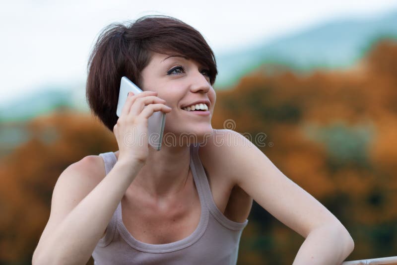 Young woman relaxing outdoors chatting on a mobile phone looking up with a happy smile as she listens to the call. Young woman relaxing outdoors chatting on a mobile phone looking up with a happy smile as she listens to the call