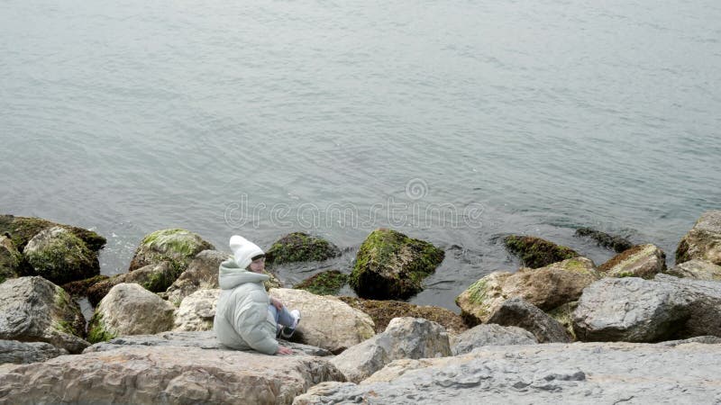 Młoda kobieta siedząca na kamieniach na wybrzeżu i patrząca na fale wodne. turysta siedzący na brzegu morza kamiennego