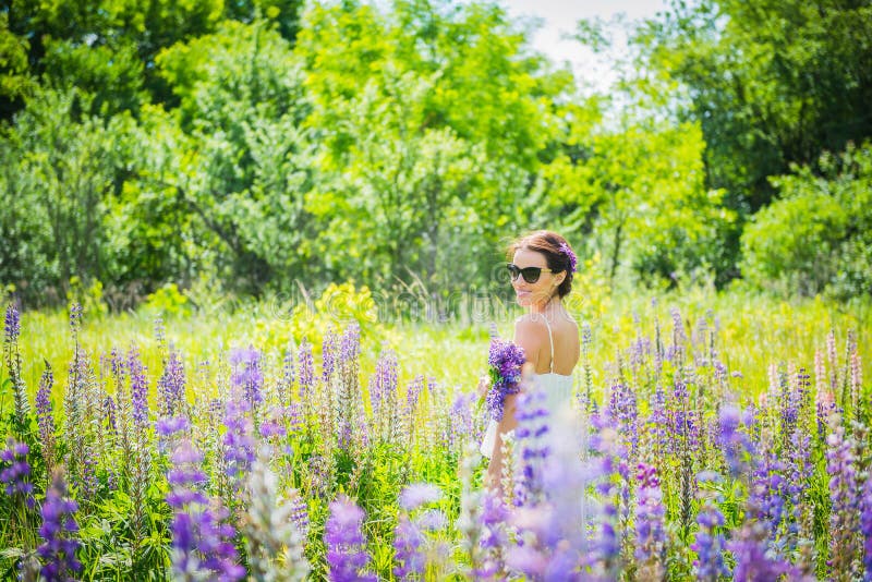 Młoda kobieta, szczęśliwa, pozycja wśród pola fiołkowi lupines, ono uśmiecha się, purpura kwitnie Niebieskie niebo na tle Lato, z zdjęcia royalty free Młoda kobieta, szczęśliwa, pozycja wśród pola fiołkowi lupines, ono uśmiecha się, purpura kwitnie Niebieskie niebo na tle Lato, z zdjęcia royalty free