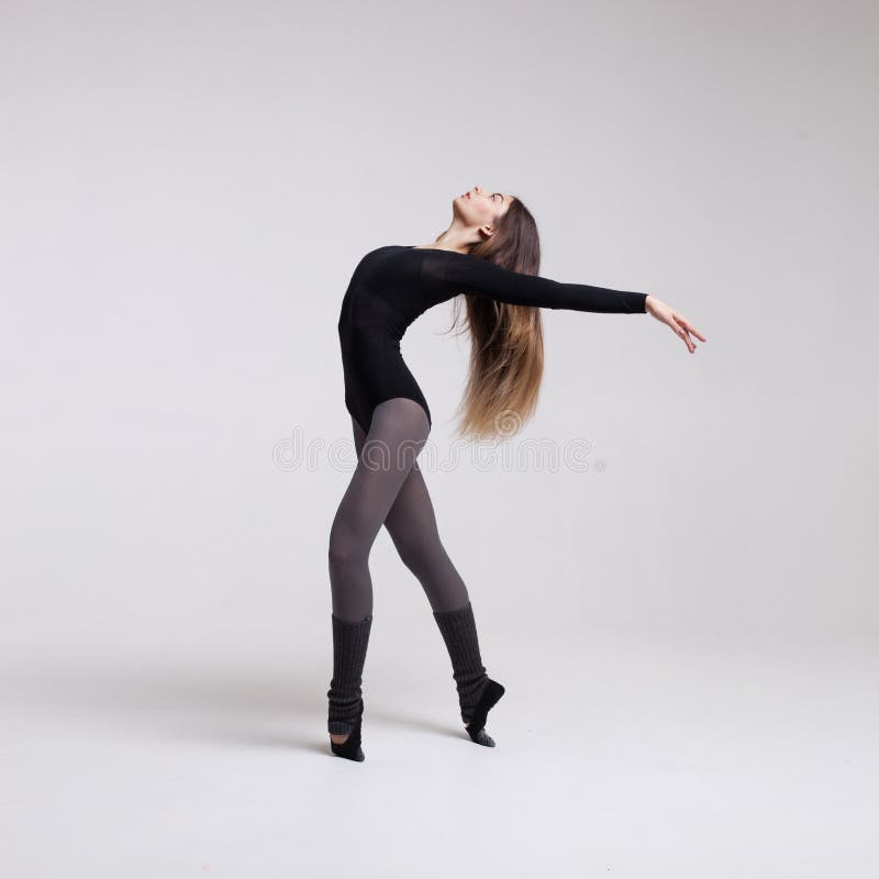 Young beautiful woman dancer with long brown hair wearing black swimsuit posing on a light grey studio background. Young beautiful woman dancer with long brown hair wearing black swimsuit posing on a light grey studio background