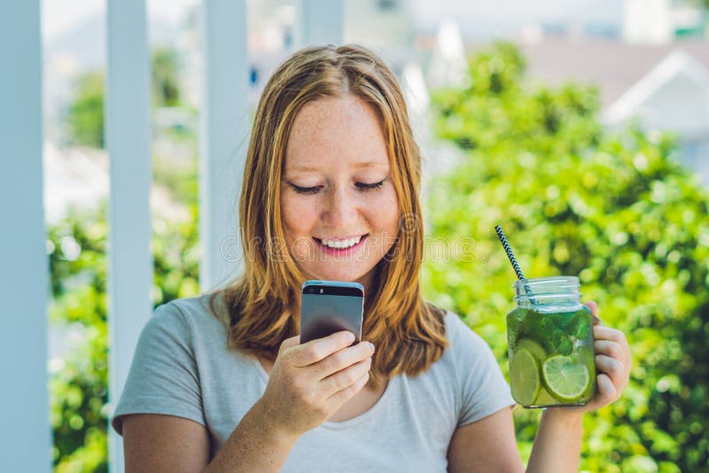 Młoda kobieta trzyma kamieniarza słój w jej ręce z mojito i smartphone Wiosna napoju pojęcie fotografia royalty free Młoda kobieta trzyma kamieniarza słój w jej ręce z mojito i smartphone Wiosna napoju pojęcie fotografia royalty free