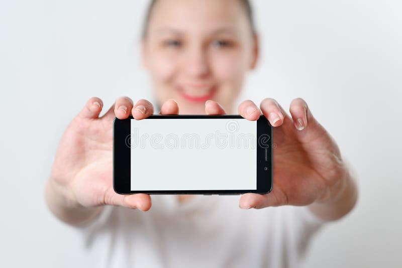 Młoda kobieta trzyma smartphone horizontally z białym ekranem z miejscem dla copyspace na lekkim tle obrazy stock Młoda kobieta trzyma smartphone horizontally z białym ekranem z miejscem dla copyspace na lekkim tle obrazy stock