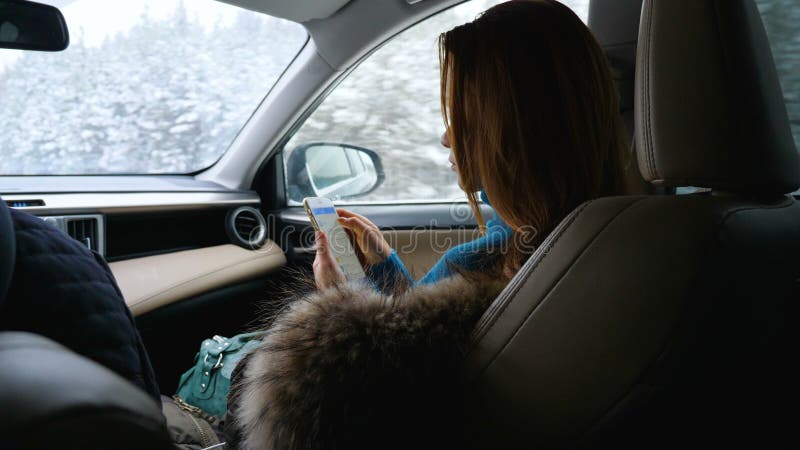 Młoda kobieta używa telefon komórkowego w frontowym miejsce pasażera w samochodzie podczas gdy siedzący