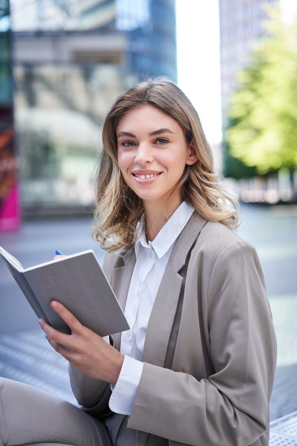 A young woman in corporate suit, sits with notebook and pen, takes notes, works and writes down her ideas. A young woman in corporate suit, sits with notebook and pen, takes notes, works and writes down her ideas.