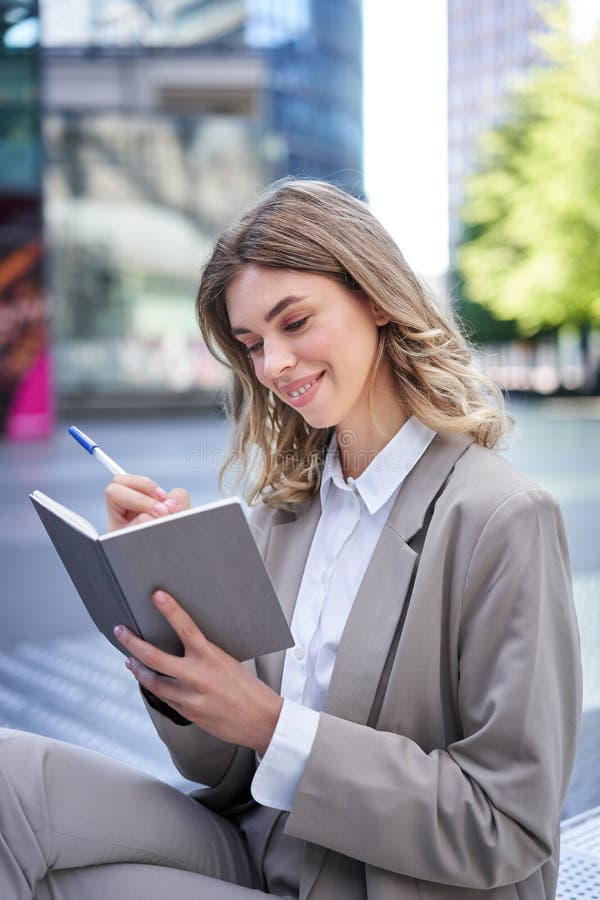 A young woman in corporate suit, sits with notebook and pen, takes notes, works and writes down her ideas. A young woman in corporate suit, sits with notebook and pen, takes notes, works and writes down her ideas.