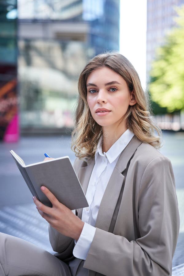 A young woman in corporate suit, sits with notebook and pen, takes notes, works and writes down her ideas. A young woman in corporate suit, sits with notebook and pen, takes notes, works and writes down her ideas.