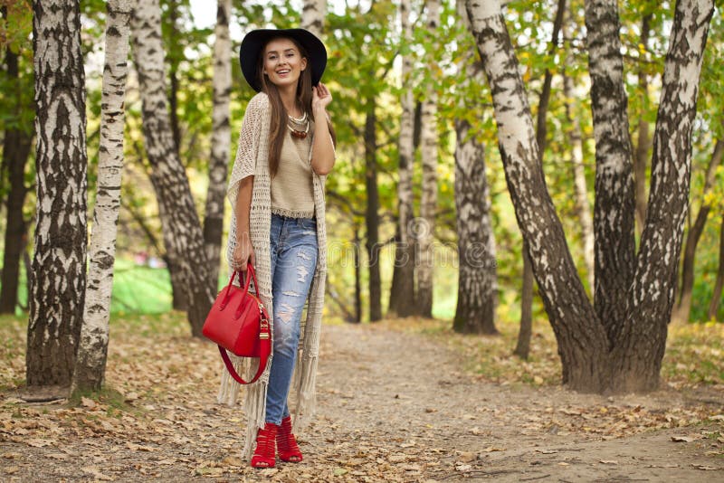 Młoda kobieta w moda niebieskich dżinsach i czerwony torby odprowadzenie w jesieni