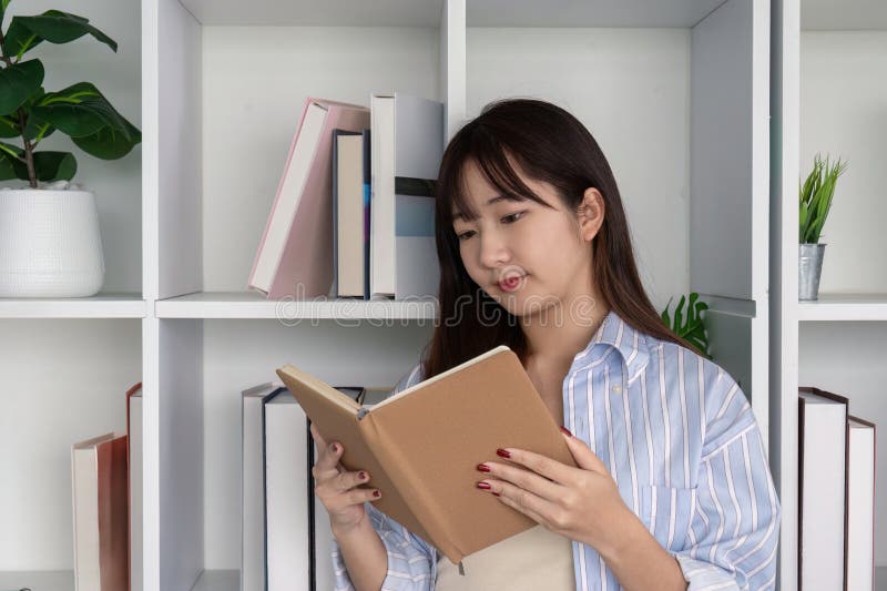 Młoda kobieta zanurzona w książce do czytania w bibliotece domowej fotografia stock