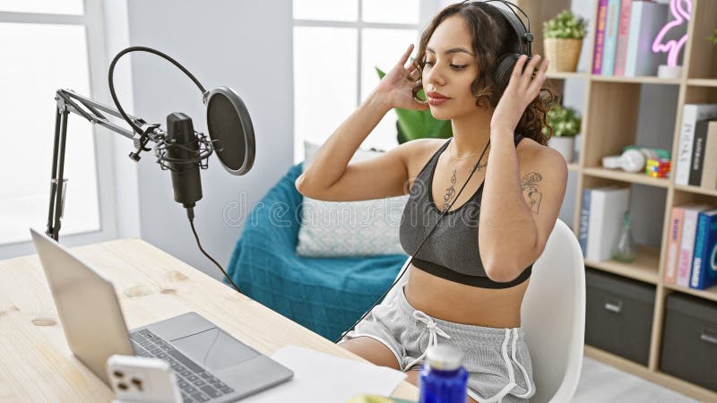 Młoda kobieta ze słuchawkami nagrywającymi podcast w nowoczesnym studio wnętrzu promieniującym kreatywnością i profesjonalizmem obraz stock