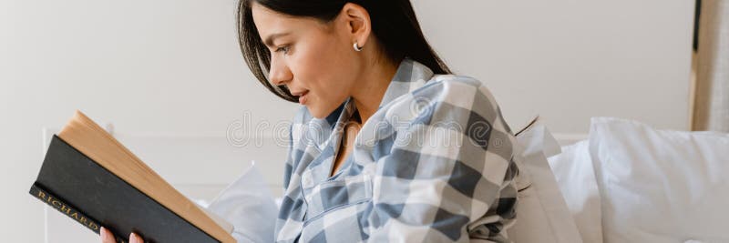 Młoda latynoska kobieta czytająca książkę leżąc w domu