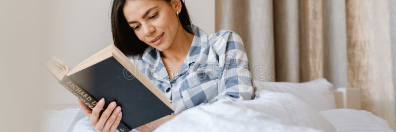 Młoda latynoska kobieta czytająca książkę leżąc w łóżku