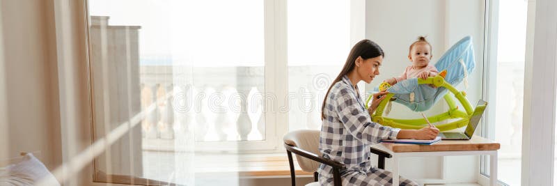 Młoda matka pracująca z laptopem, trzymająca dziecko w domu