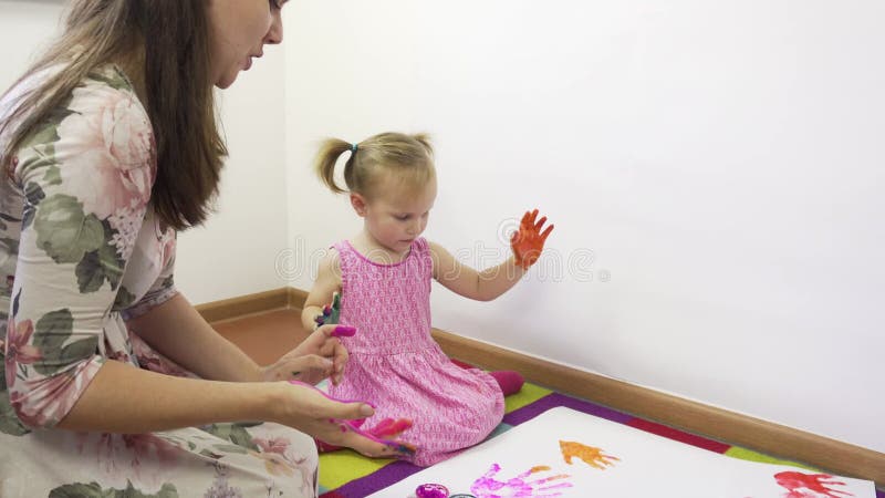 Młoda matka z piękną córką rysuje z farbami palcami.