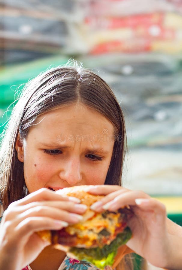 Młoda nastoletnia dziewczyna je hamburger Dziewczyna próbuje jeść fast food obraz royalty free Młoda nastoletnia dziewczyna je hamburger Dziewczyna próbuje jeść fast food obraz royalty free