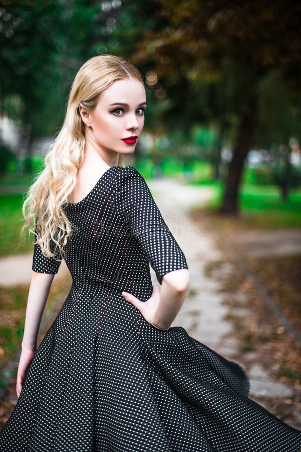 Młoda piękna blond dziewczyna z czerwoną pomadką w jej dużych jaskrawych oczach i robi mu w sukni pozuje na ulicach położenia sło zdjęcie stock Młoda piękna blond dziewczyna z czerwoną pomadką w jej dużych jaskrawych oczach i robi mu w sukni pozuje na ulicach położenia sło zdjęcie stock