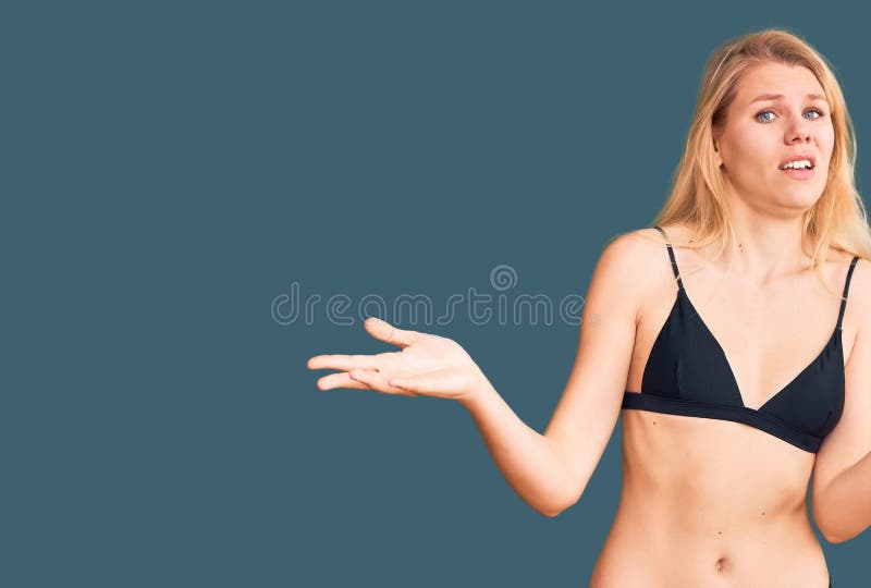 Młoda, piękna blondynka, ubrana w bikini bez skrupułów i zmieszana z otwartymi ramionami bez pojęcia zdjęcia royalty free