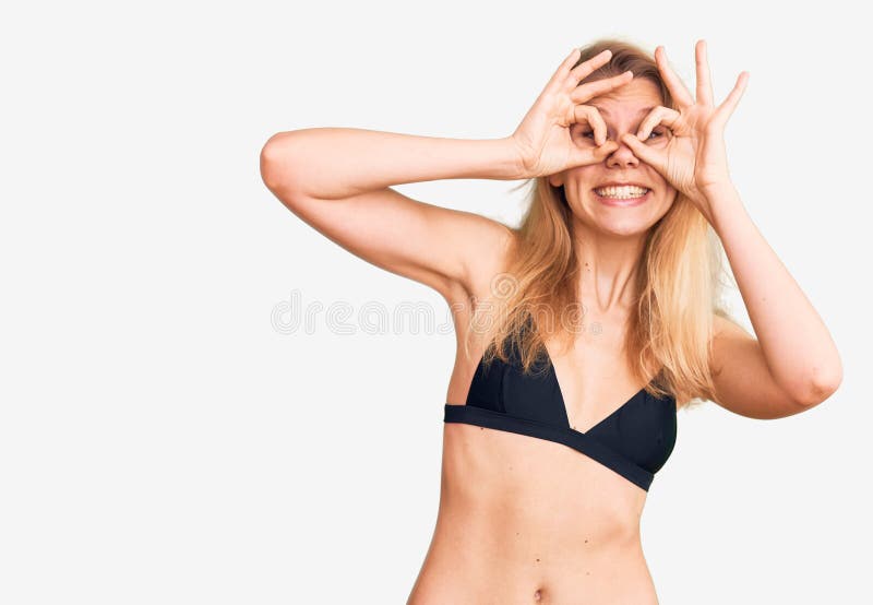 Młoda, piękna blondynka w bikini, robi niezły gest, jak lornetka, wytykająca językiem oczy patrzące przez palce fotografia royalty free