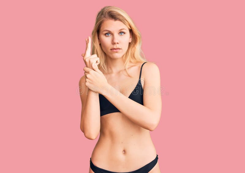 Młoda, piękna blondynka w bikini trzymająca symboliczną broń z gestem ręki grająca zabijając strzelającą broń wściekłą twarzą obrazy royalty free