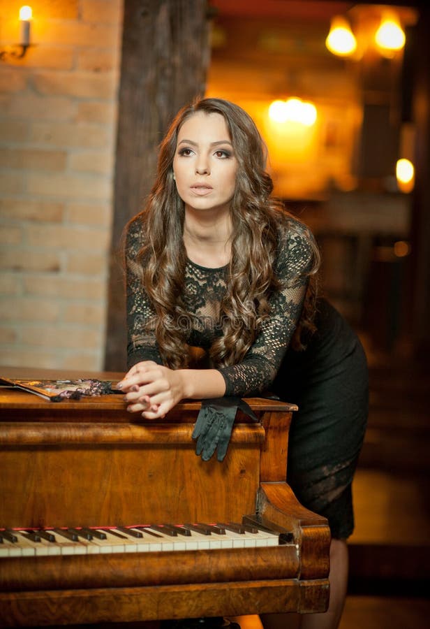 Młoda piękna brunetki kobieta w eleganckiej czerni sukni pozyci blisko rocznika pianina Zmysłowa romantyczna dama z długim ciemny fotografia royalty free Młoda piękna brunetki kobieta w eleganckiej czerni sukni pozyci blisko rocznika pianina Zmysłowa romantyczna dama z długim ciemny fotografia royalty free