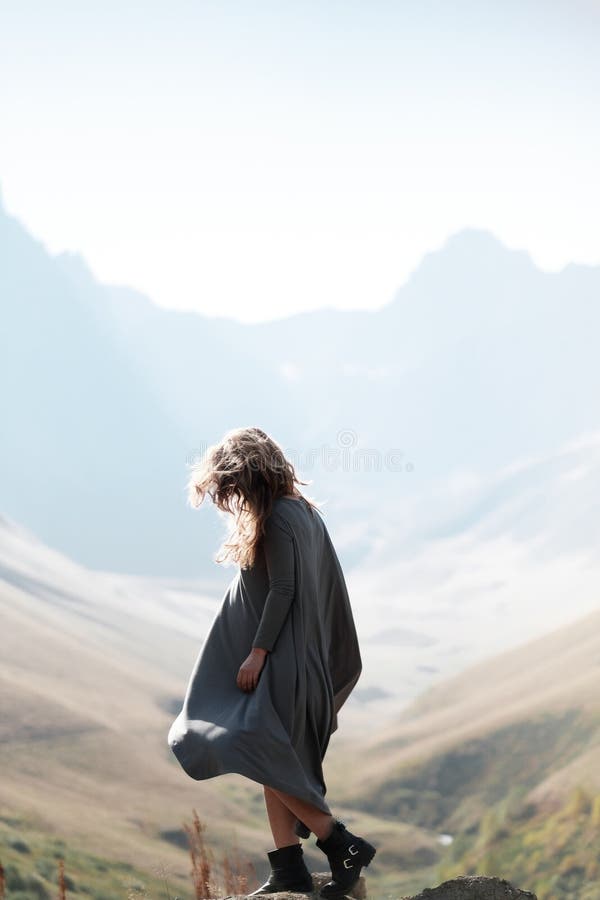 Młoda piękna dziewczyna w długiej sukni stoi falezą w tle góry fotografia stock Młoda piękna dziewczyna w długiej sukni stoi falezą w tle góry fotografia stock