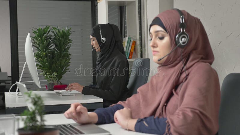 Młoda piękna dziewczyna w różowym hijab opowiada na słuchawki, odpowiada wezwania w centrum telefonicznym Arabskie kobiety w