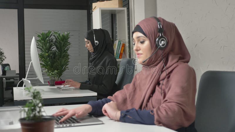 Młoda piękna dziewczyna w różowym hijab opowiada na słuchawki, odpowiada wezwania w centrum telefonicznym Arabskie kobiety w