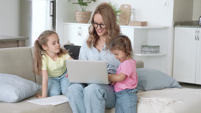 Młoda, pozytywna matka, która próbuje pracować nad laptopem z dziećmi w domu